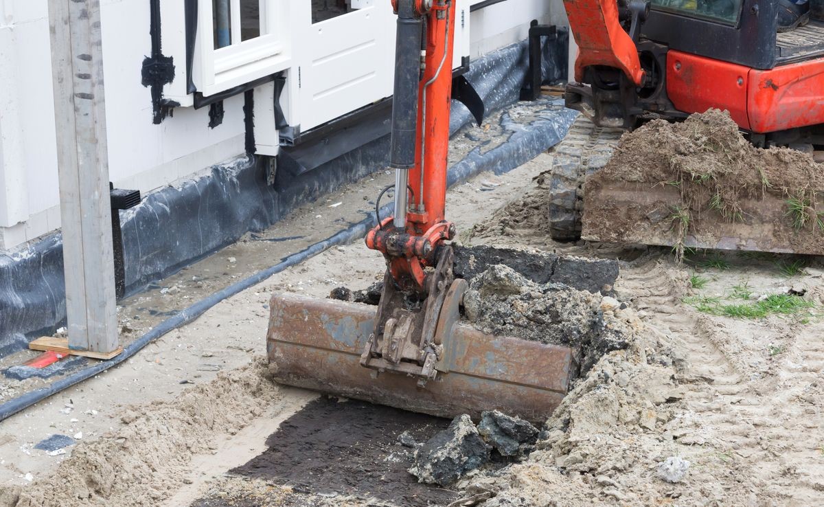 Small crane is leveling ground at a building site of a dutch house