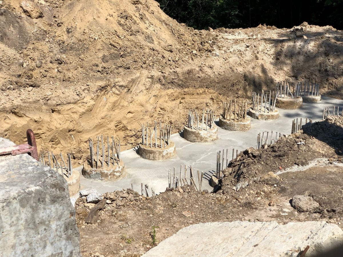 The row of concrete piles with metal rods in cemented ground for foundation in a ditch at construction site
